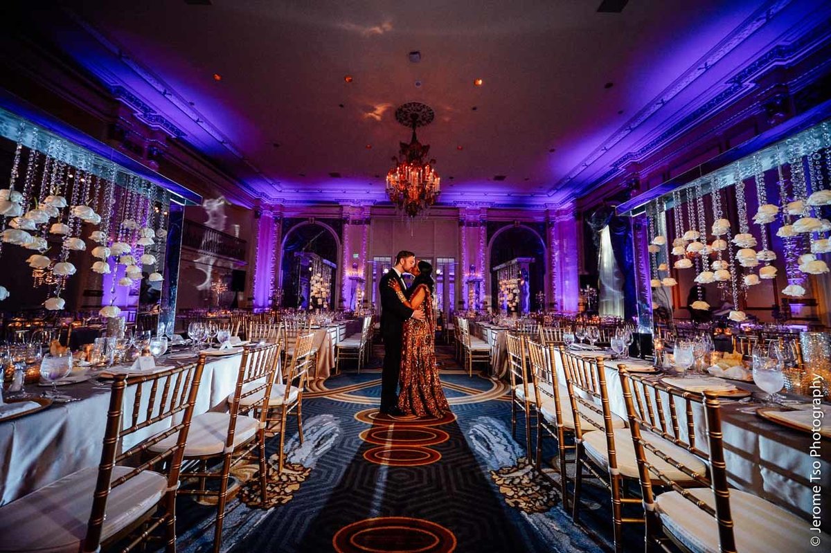 bride and groom standing in St Andrews Ballroom at Fairmont Olympic Hotel with long tables and gold Chivari chaors, and tall centerpieces with trailing roses
