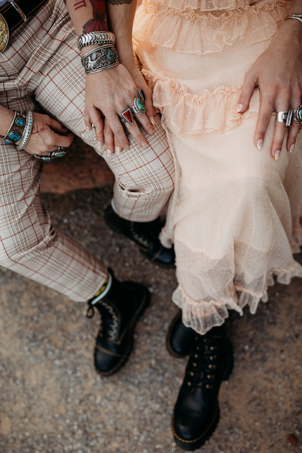 Detail shot of a couple's edgy wedding outfit, featuring leather boots and lace dress hem, with hands adorned in silver jewelry