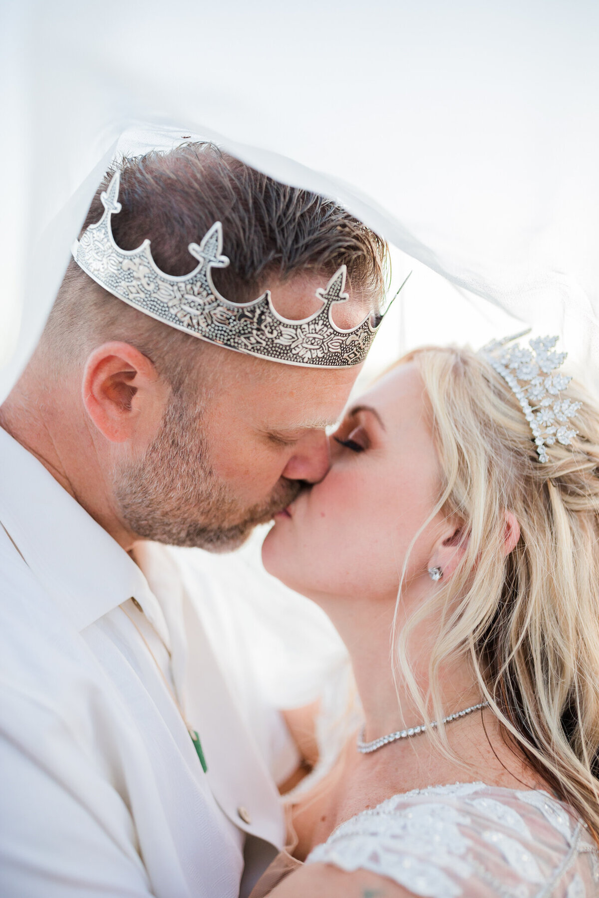 bride and groom wearing crowns under bridal veil