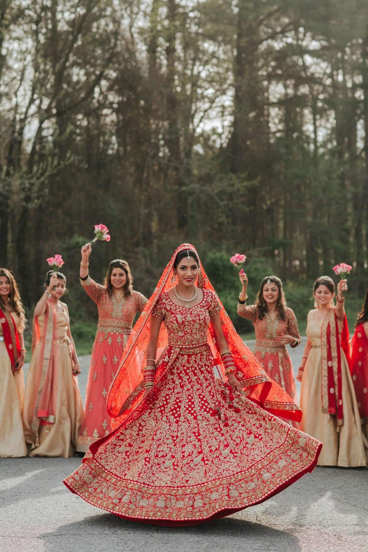 Indian bride in her red dress on the morning of her wedding day with her bride's maids. Bride is twirling as her bridesmaids cheer her.