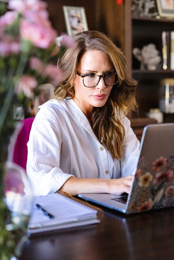 Woman with glasses works on a laptop.