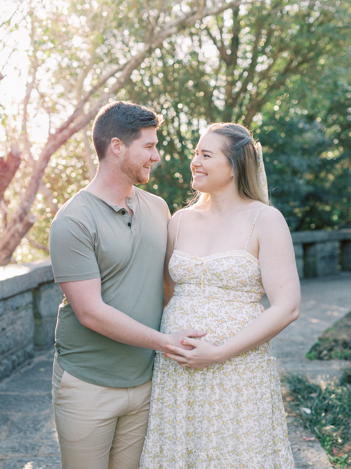 A couple smiling at each other while holding the mother's pregnancy bump during a Richmond maternity photography session by Katie Stansfield Photography.