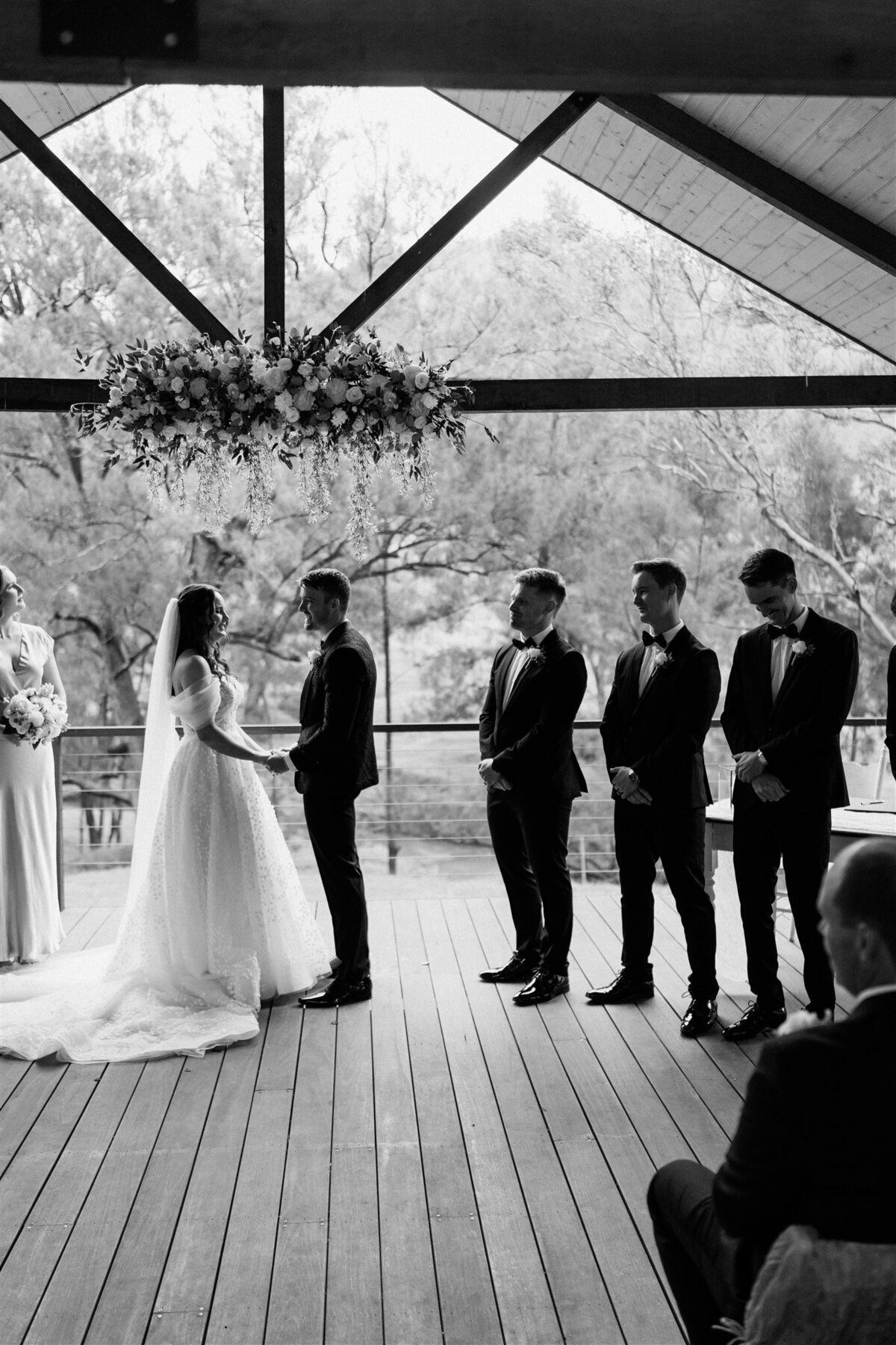 A beaming bride, clutching a bouquet of white roses, exchanges vows with her groom under a canopy of fragrant blossoms.