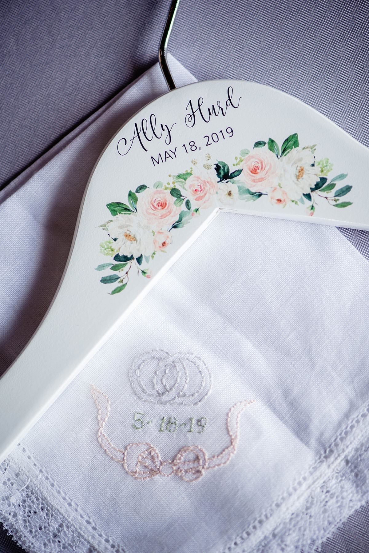 Custom white wedding hanger with flowers and calligraphy name sitting on top of a white embroidered handkerchief