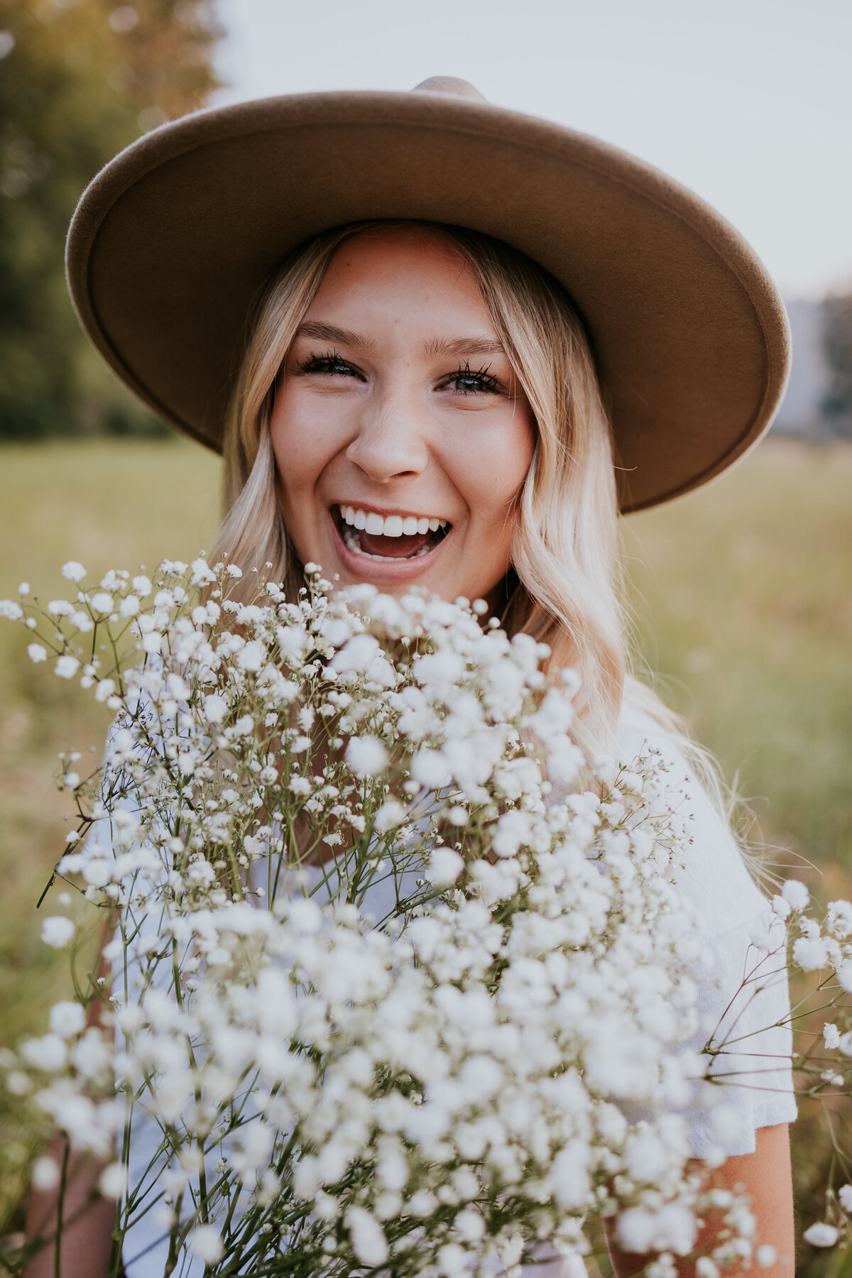 Young woman laughs behind bouquet of babies breath flowers.
