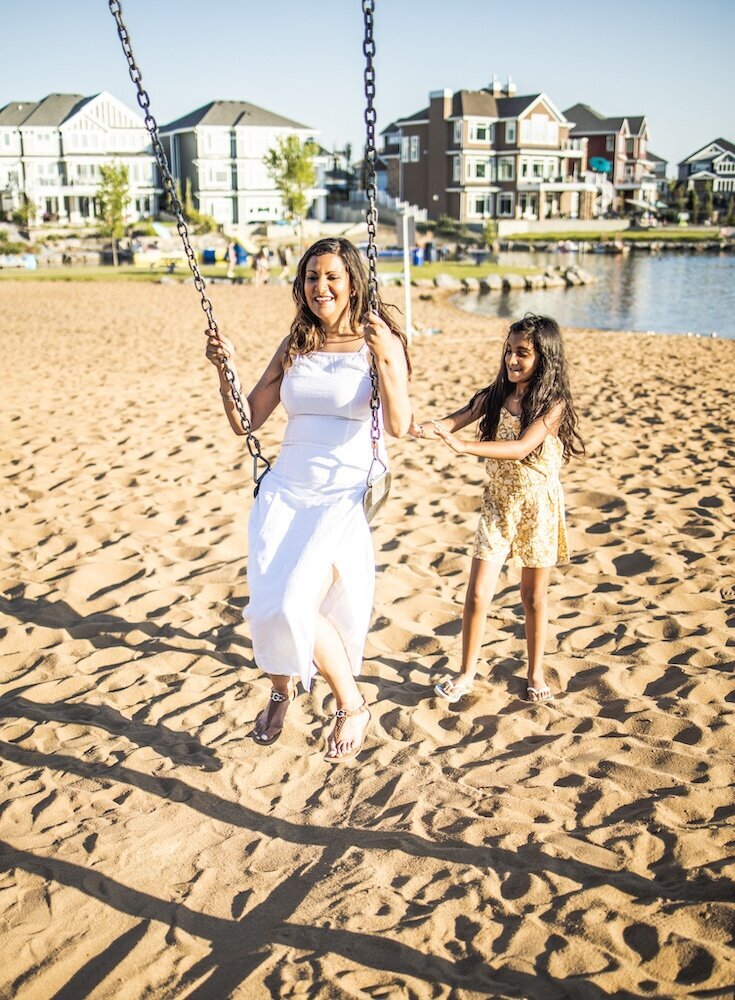 A little girl pushes her mom on the swing