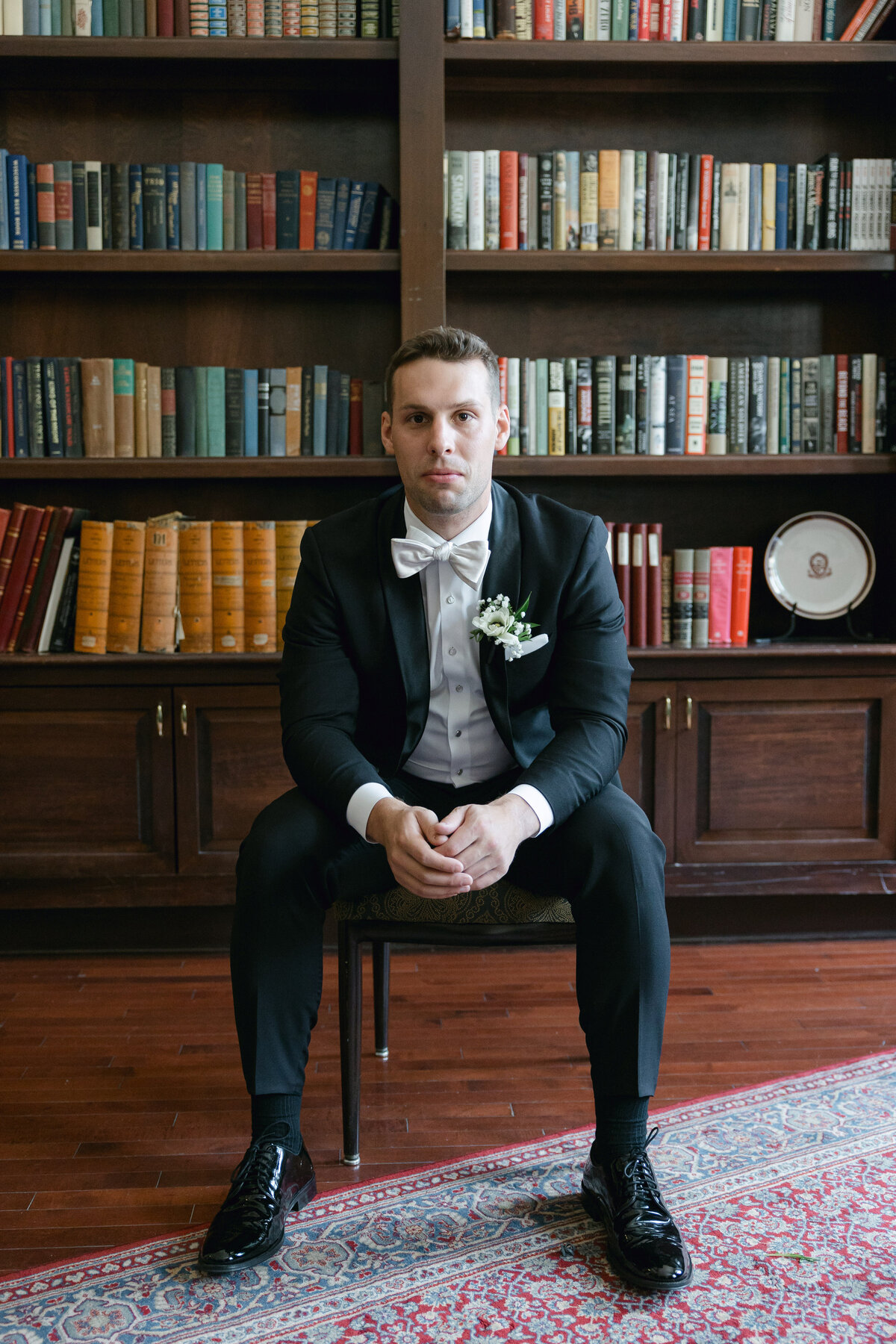A stylish portrait of the groom sitting in a chair in the library at The Madison Club, showcasing his elegance and the venue's sophisticated ambiance.
