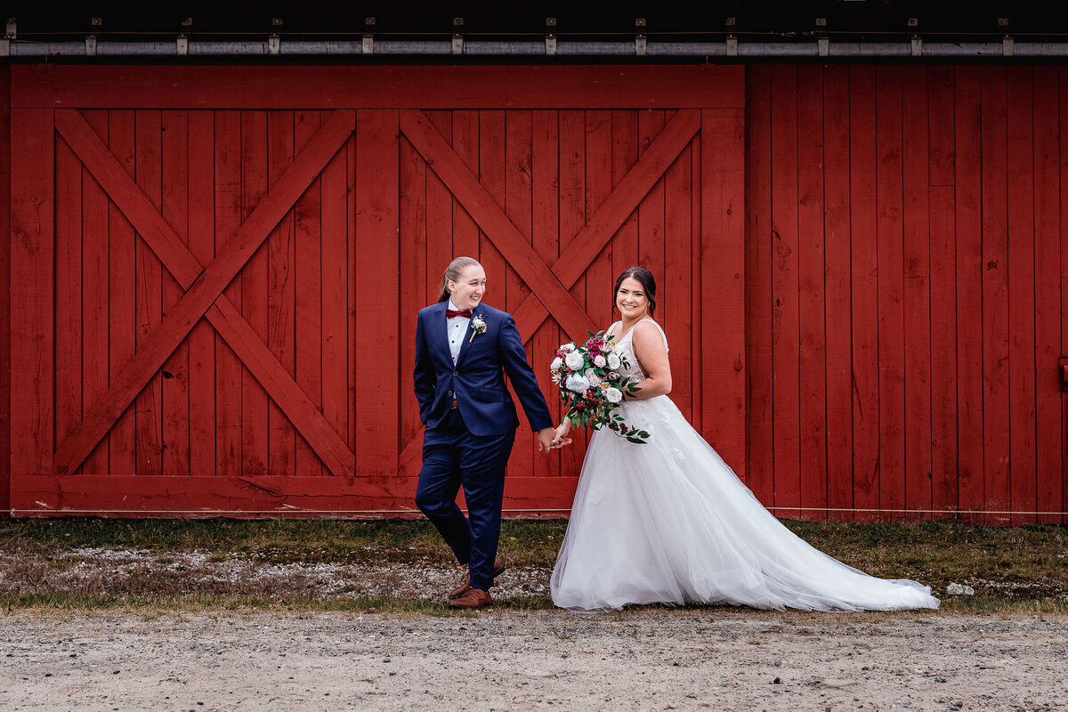 gay couple walks in front of big red barn in town square at Waterville Valley Resort wedding by Lisa Smith Photography