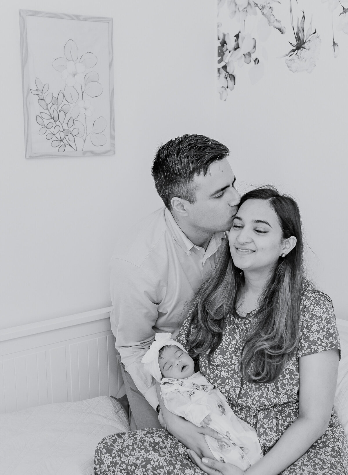 Black and white lifestyle newborn photography featuring a loving couple holding their sleeping baby girl. This intimate family moment highlights the joy of welcoming a newborn at home