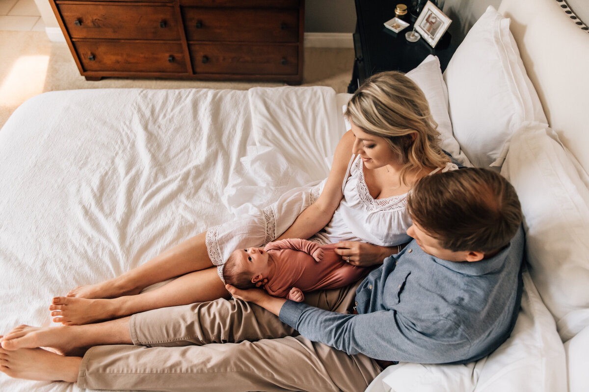 Newborn Photographer, Dad and mom snuggling baby on their bed.