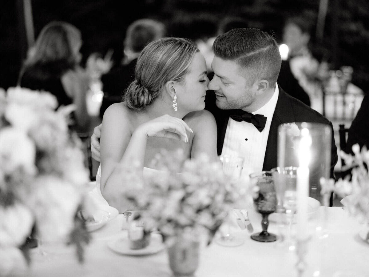 The bride and the groom are seated close, noses touching, at the elegant wedding reception. Image by Jenny Fu Studio