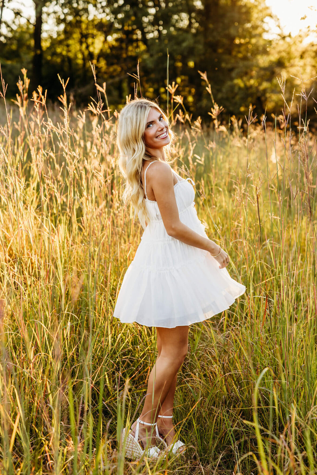 stunning blonde high school girl playing with her dress in a field at sunset