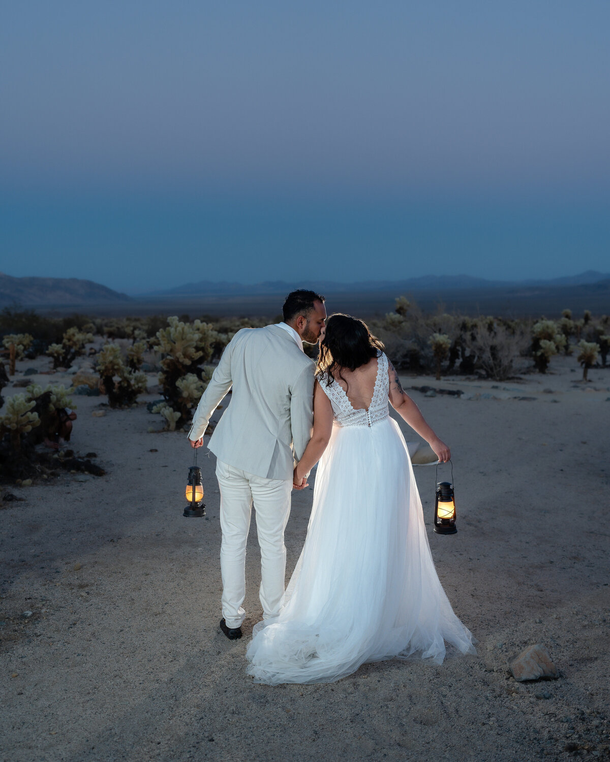 Joshua Tree elopement with bride and groom at Cholla Cactus Garden kissing while holding lanterns.