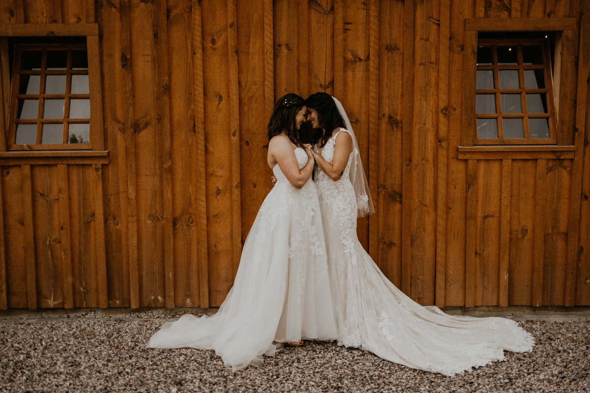 two brides standing in front of a barn in their wedding dresses