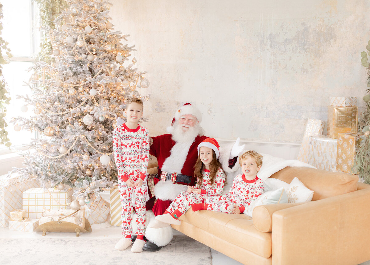santa smiles at the camera with three children wearing holiday pajamas