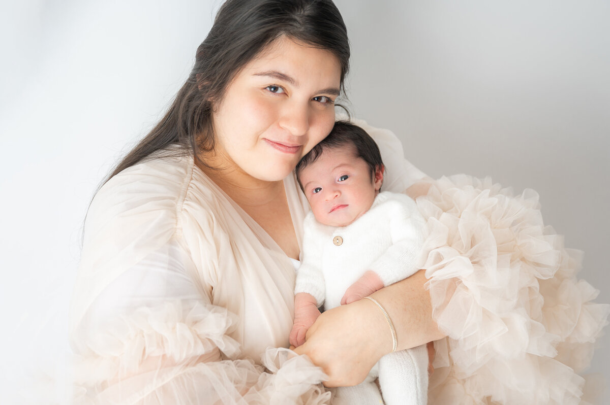 Mother in a light beige robe and newborn baby snuggled close.