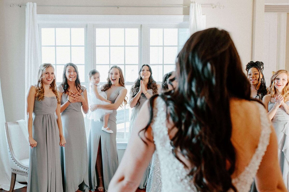Bridesmaids react happily to bride's wedding dress reveal.
