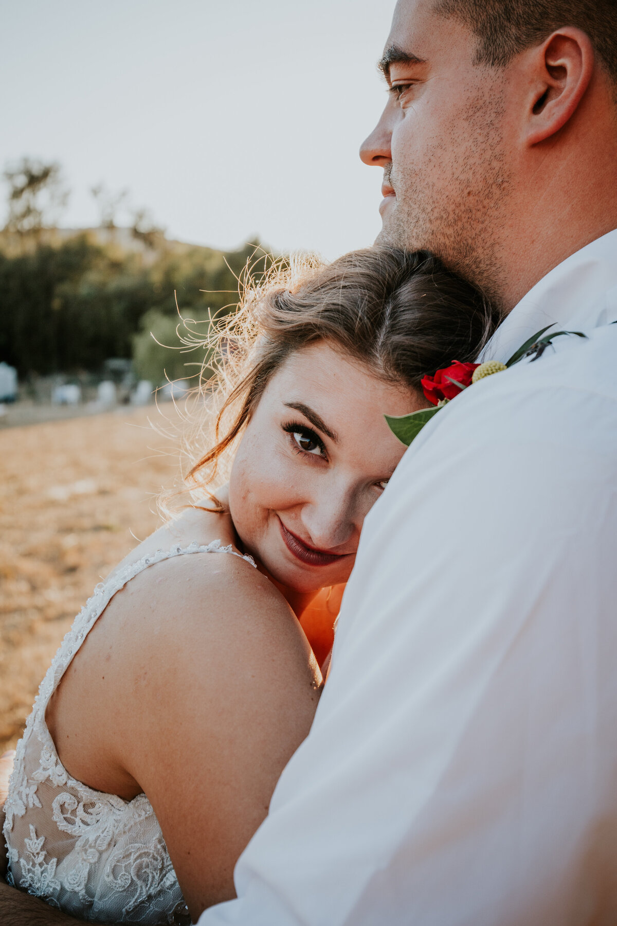 Bride leans into grooms chest hugging him and she looks at the camera sweetly.