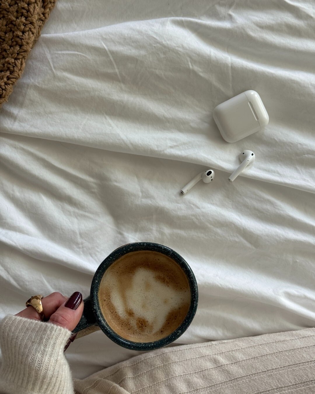 female influencer assistant sitting on her bed drinking coffee with her white airpods