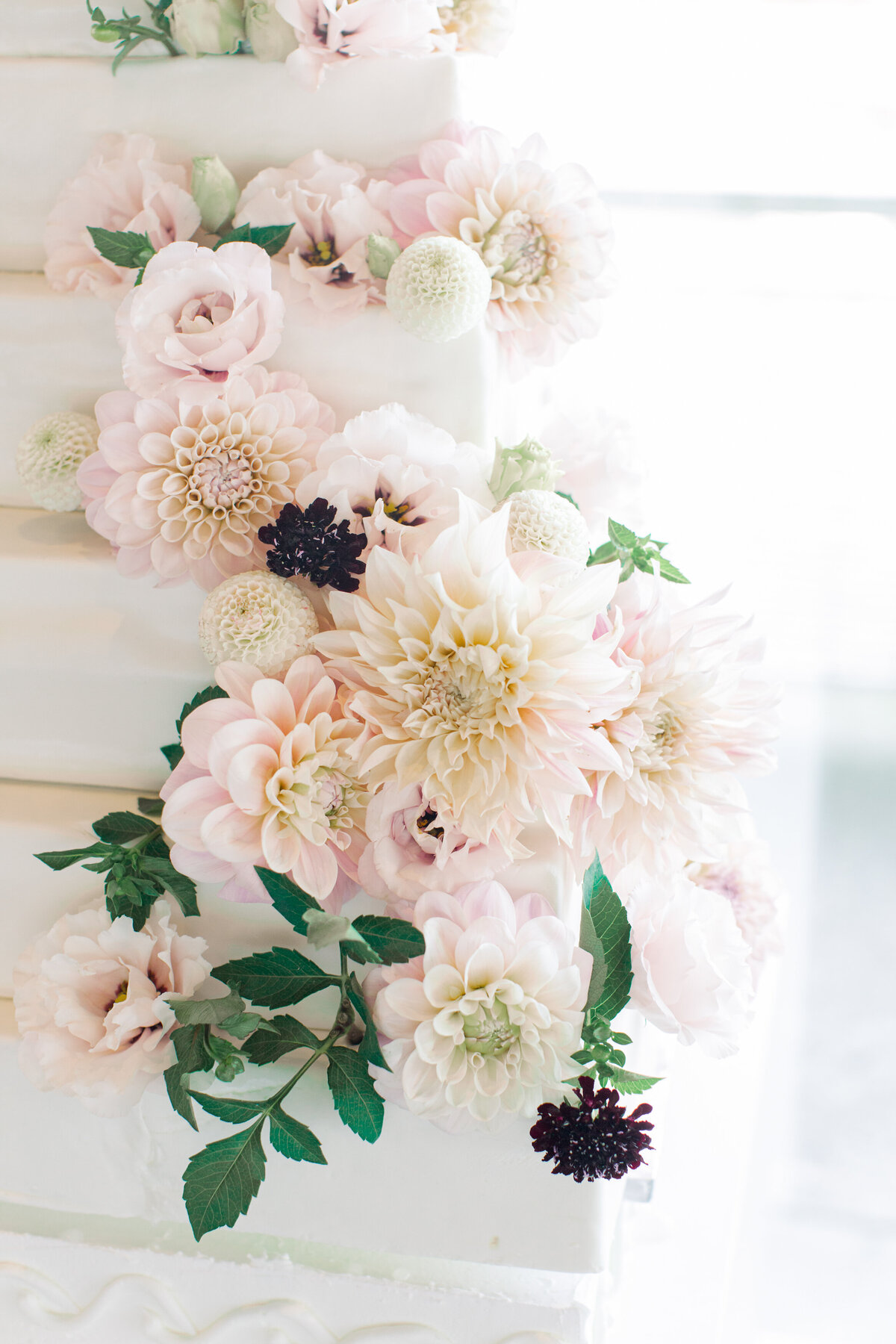 A large tiered cake decorated with pale pink flowers and leaves at a Montreal wedding.