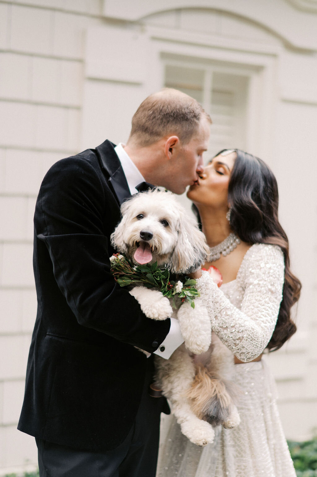 Bride and groom kiss while holding their dog with a greenery floral collar during portraits at Old Edwards Inn.
