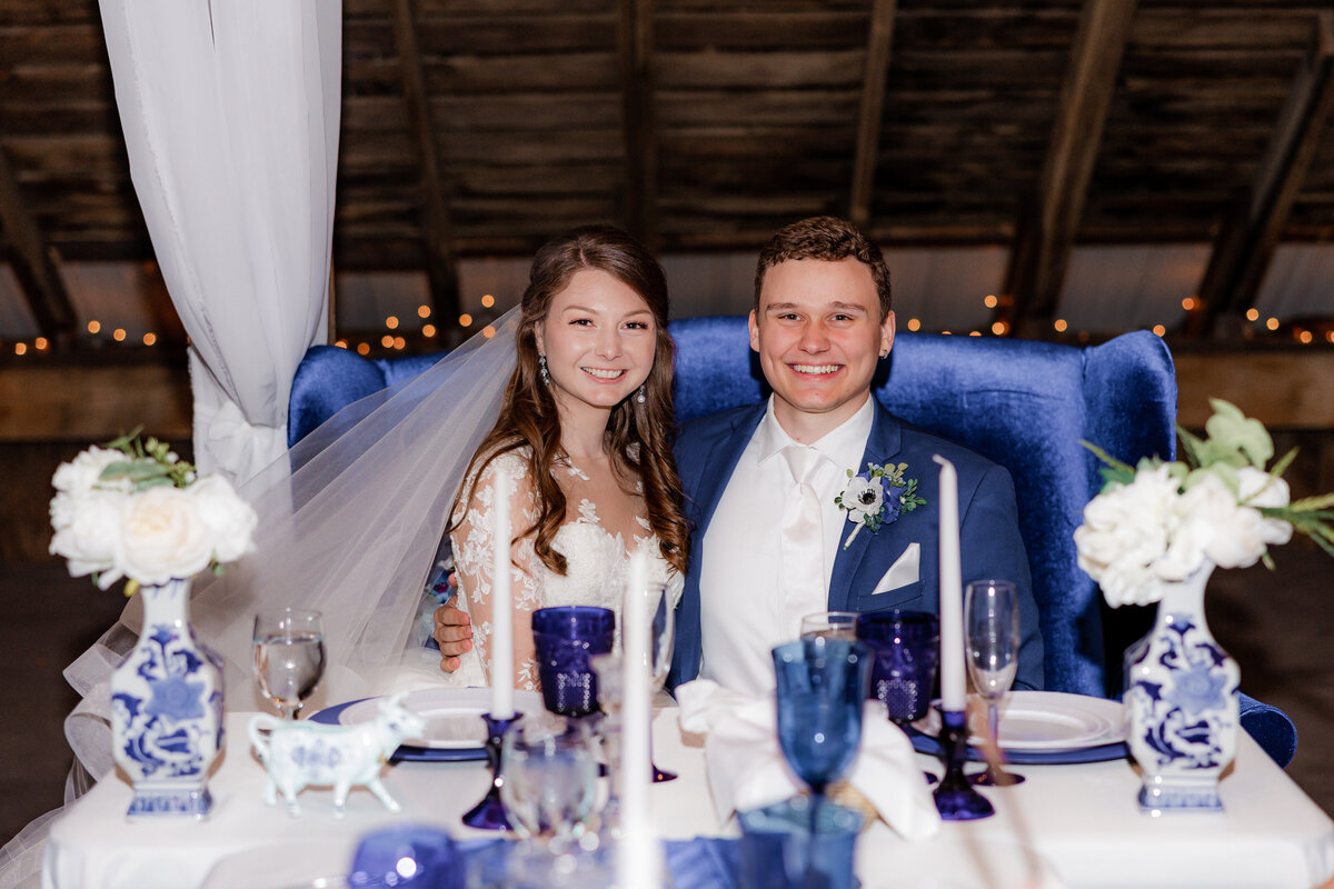 Wedding couple sit on a velvet blue couch for a portrait by Sheena Anne Photography