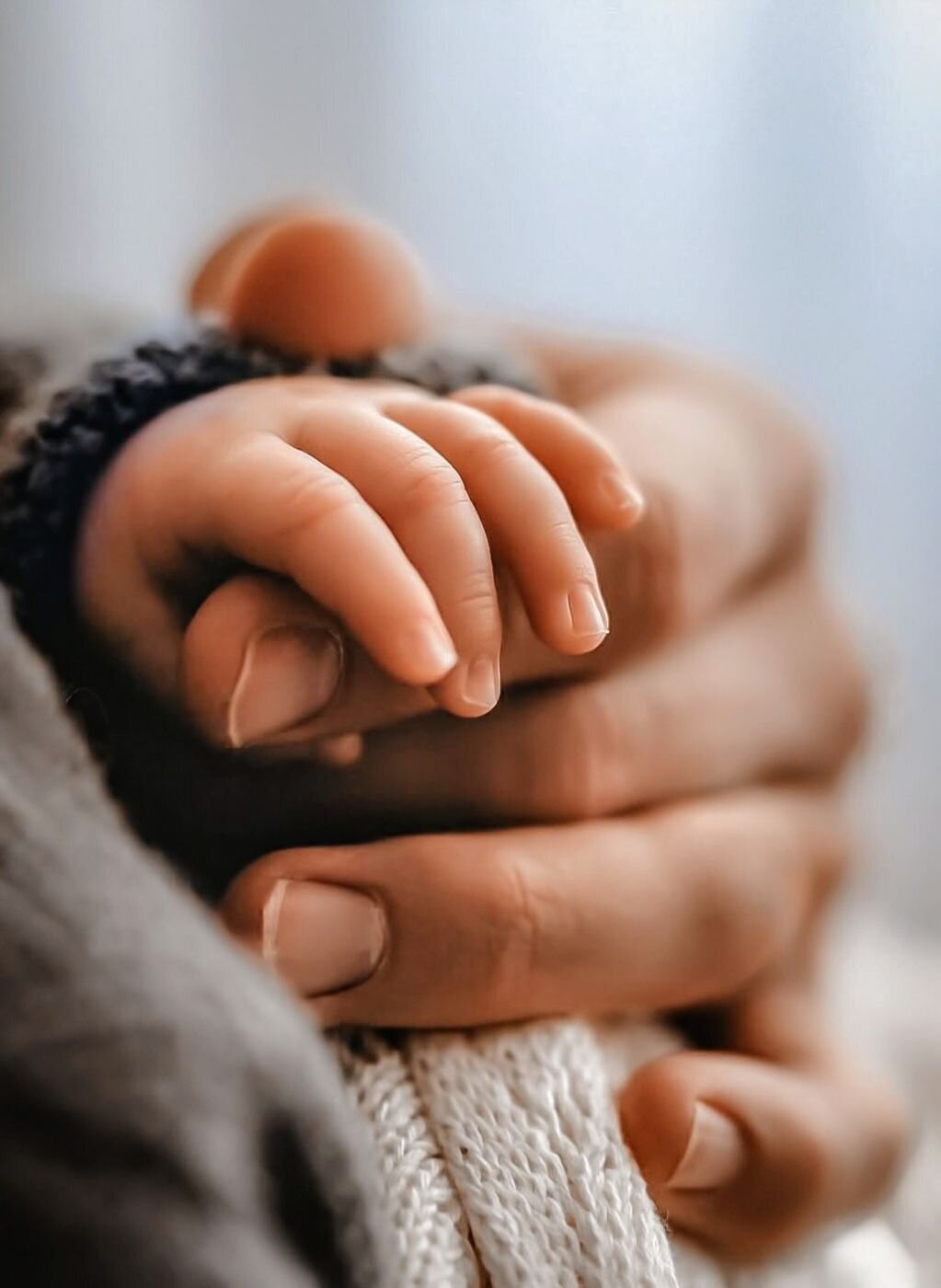 De hand van een volwassene omvat zachtjes de hand van een pasgeboren baby