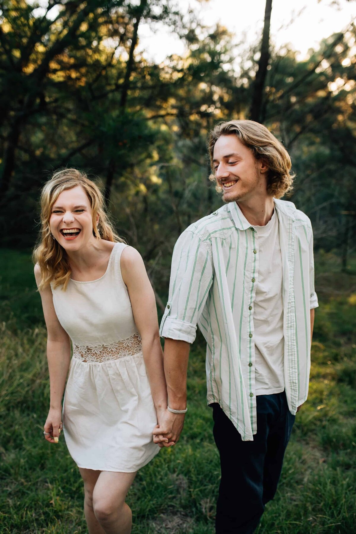 Young couple holding hands and laughing during outdoor couple photoshoot, by Delanie, Couple Photography Melbourne