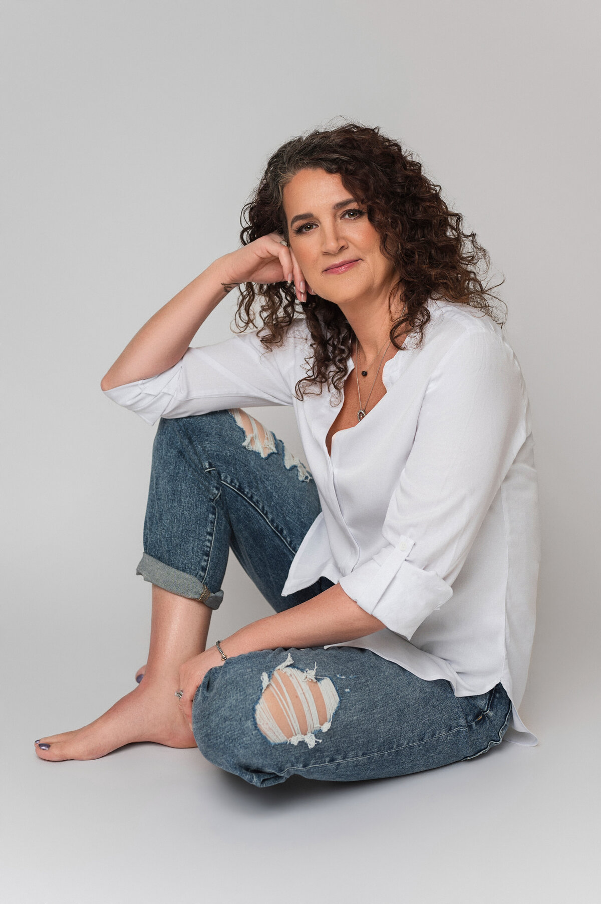 Relaxed and natural portrait of a woman in a white blouse and ripped jeans, captured by Leslie Q Photography