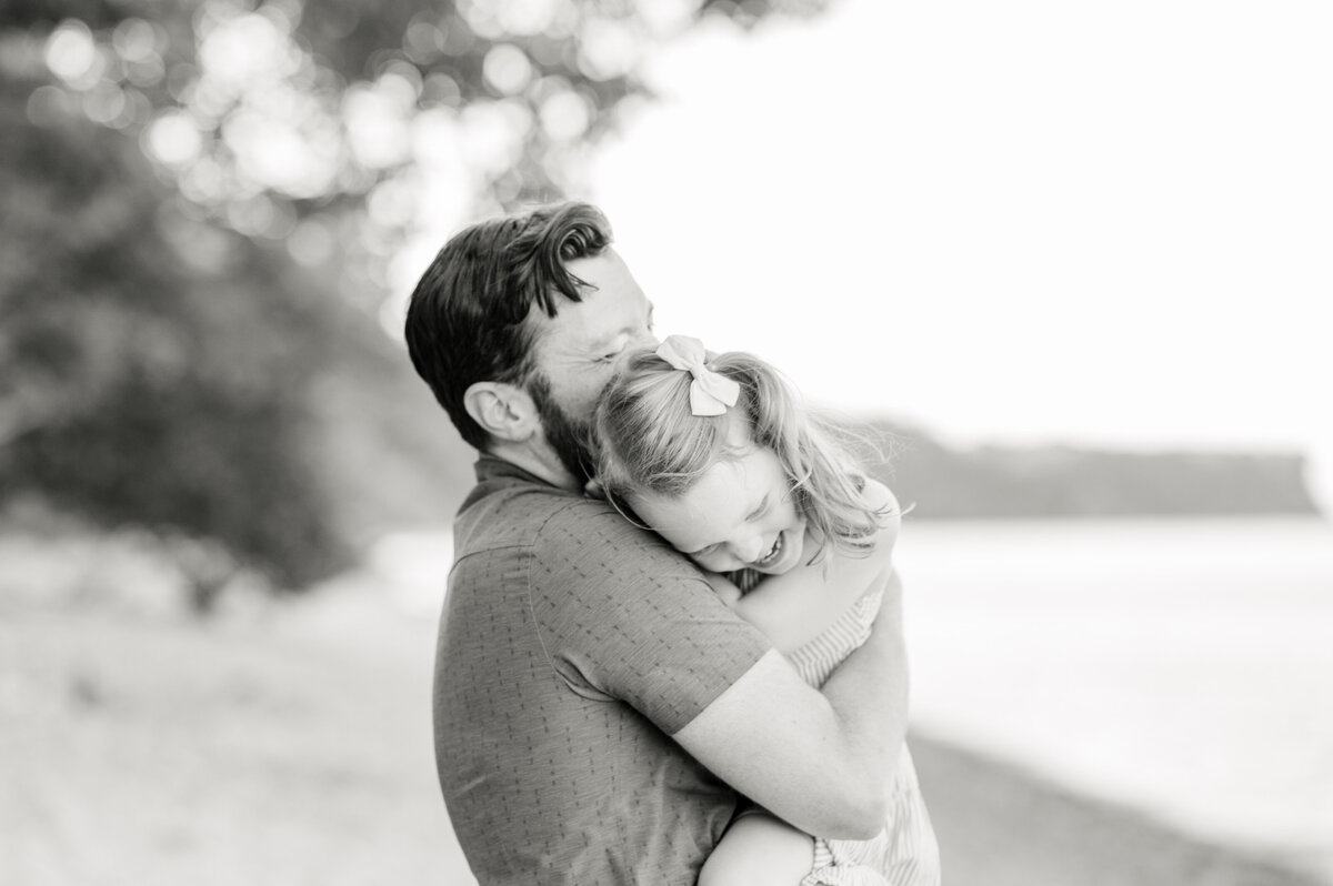 Black and white image of a dad snuggling his daughter against his chest