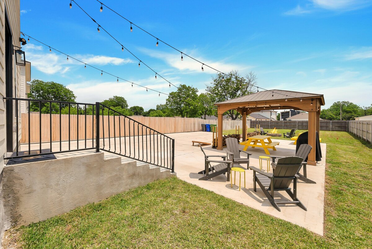 Spacious, fenced-in backyard entertainment area with patio seating and lighting at this four-bedroom, 4.5 bathroom new construction vacation rental house with free wifi, fire pit, gazebo, cornhole, private bathrooms for each bedroom within walking distance of Magnolia and Baylor in downtown Waco, TX.