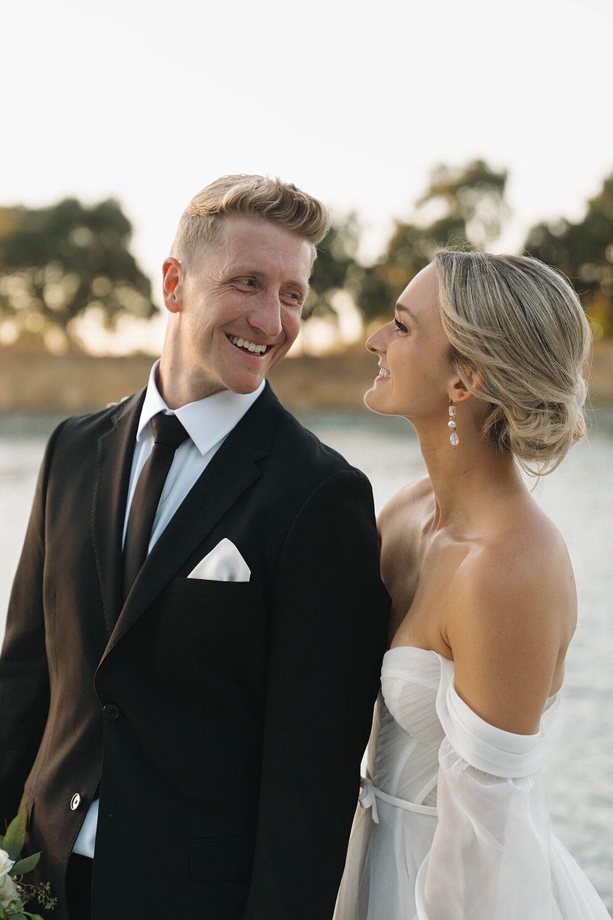 Groom laughing with his bride at sunset by the water