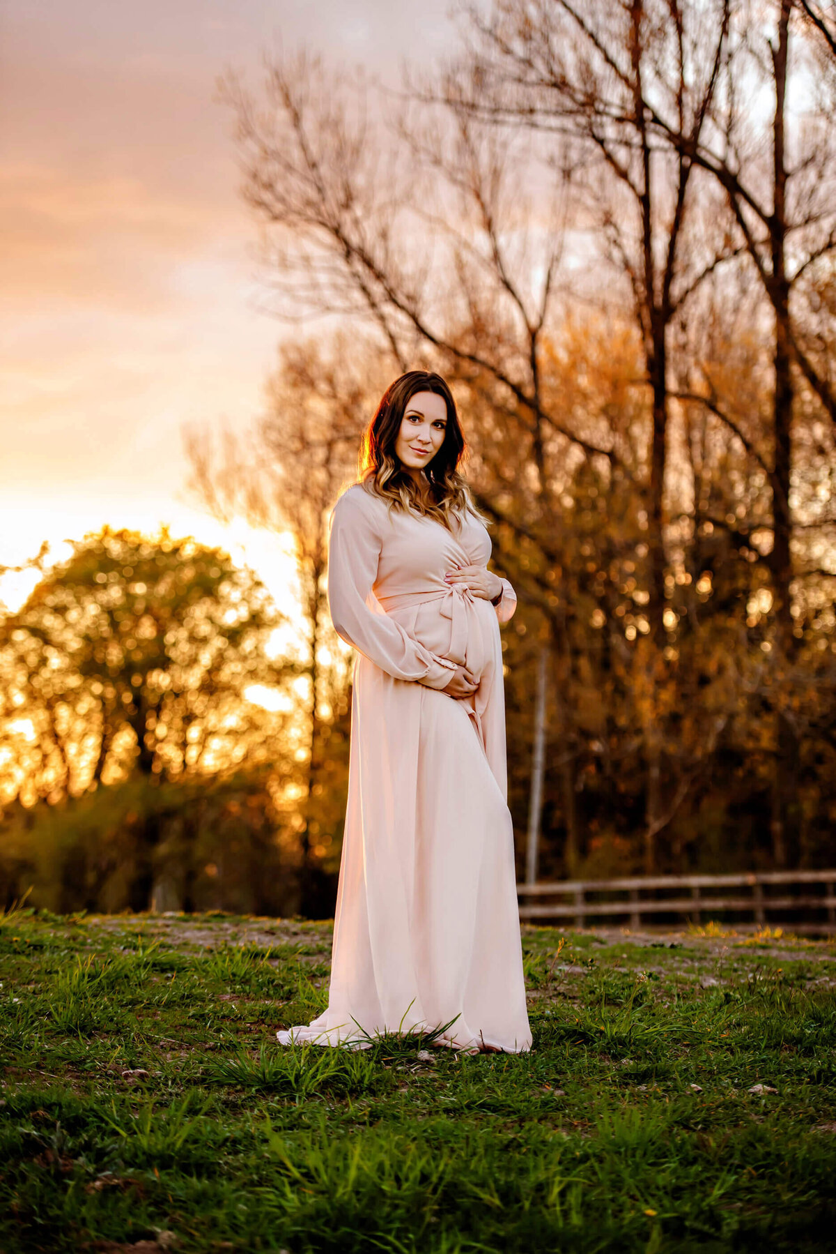 pregnant woman holding her belly with the golden hour sun behind her for her maternity photos 