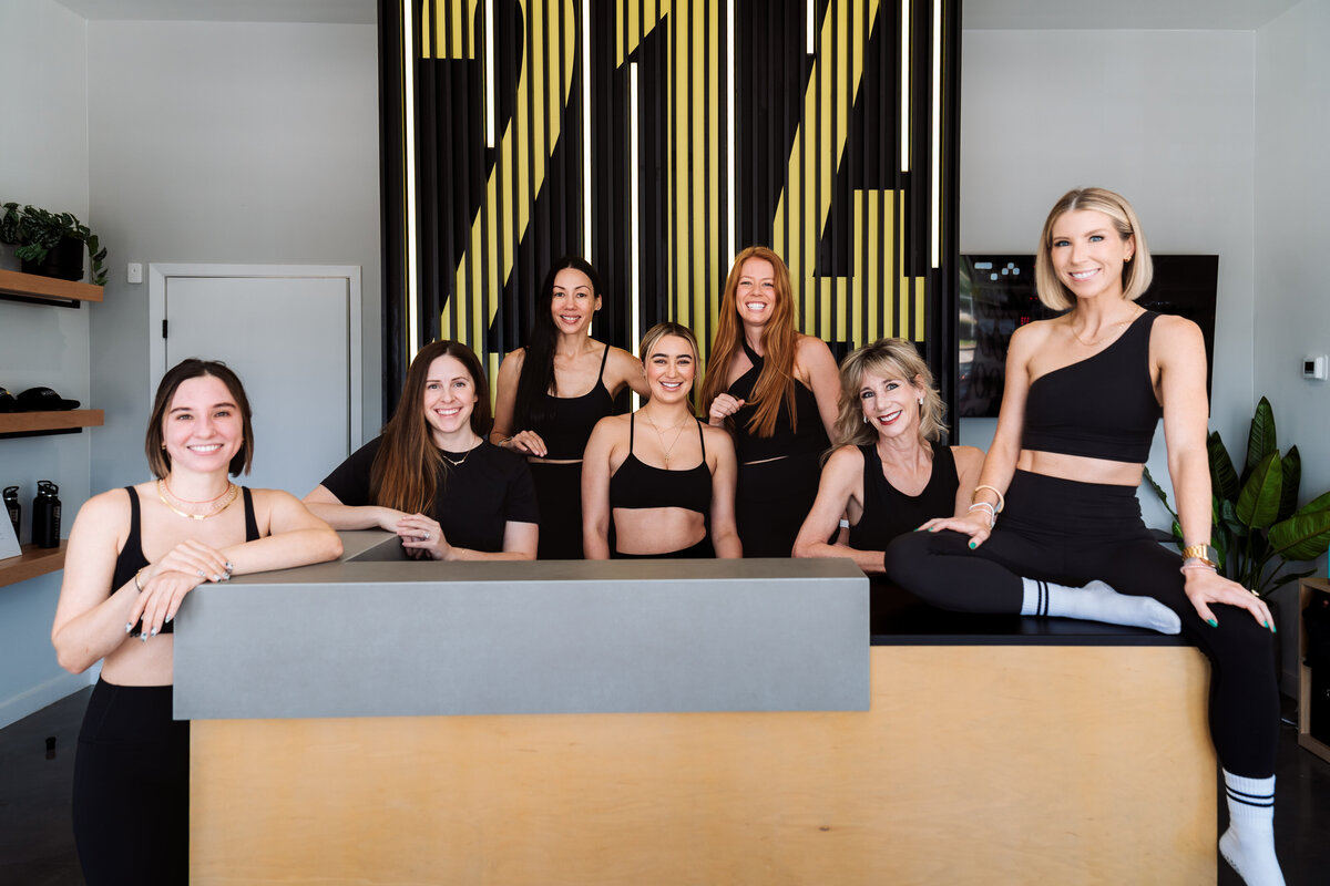 Group of Pilates214 Pilates instructors standing in front of neon I Leveled Up with Pilates214 sign in Dallas studio.