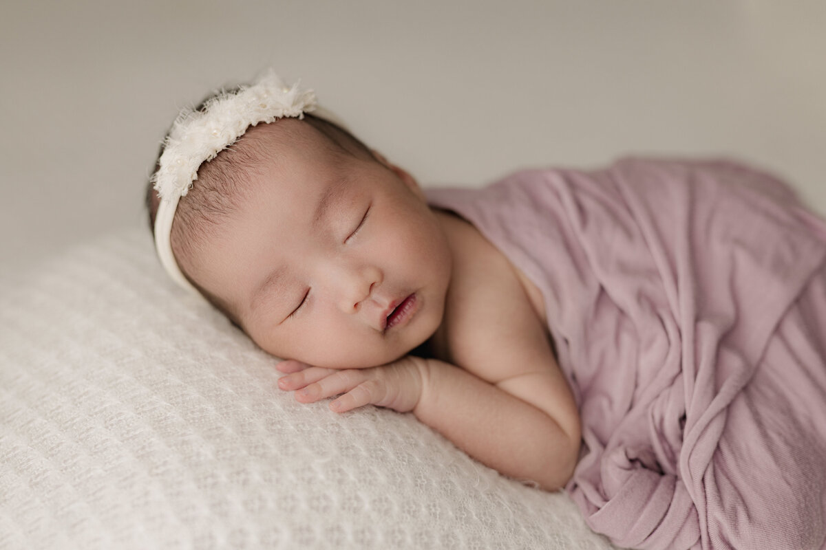 baby laying on white backdrop with pink wrap covering her back