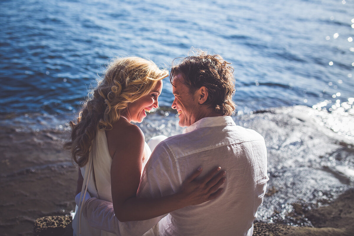 A bride and groom smiling at one another on the rocky cliffs on Gabriola Island.