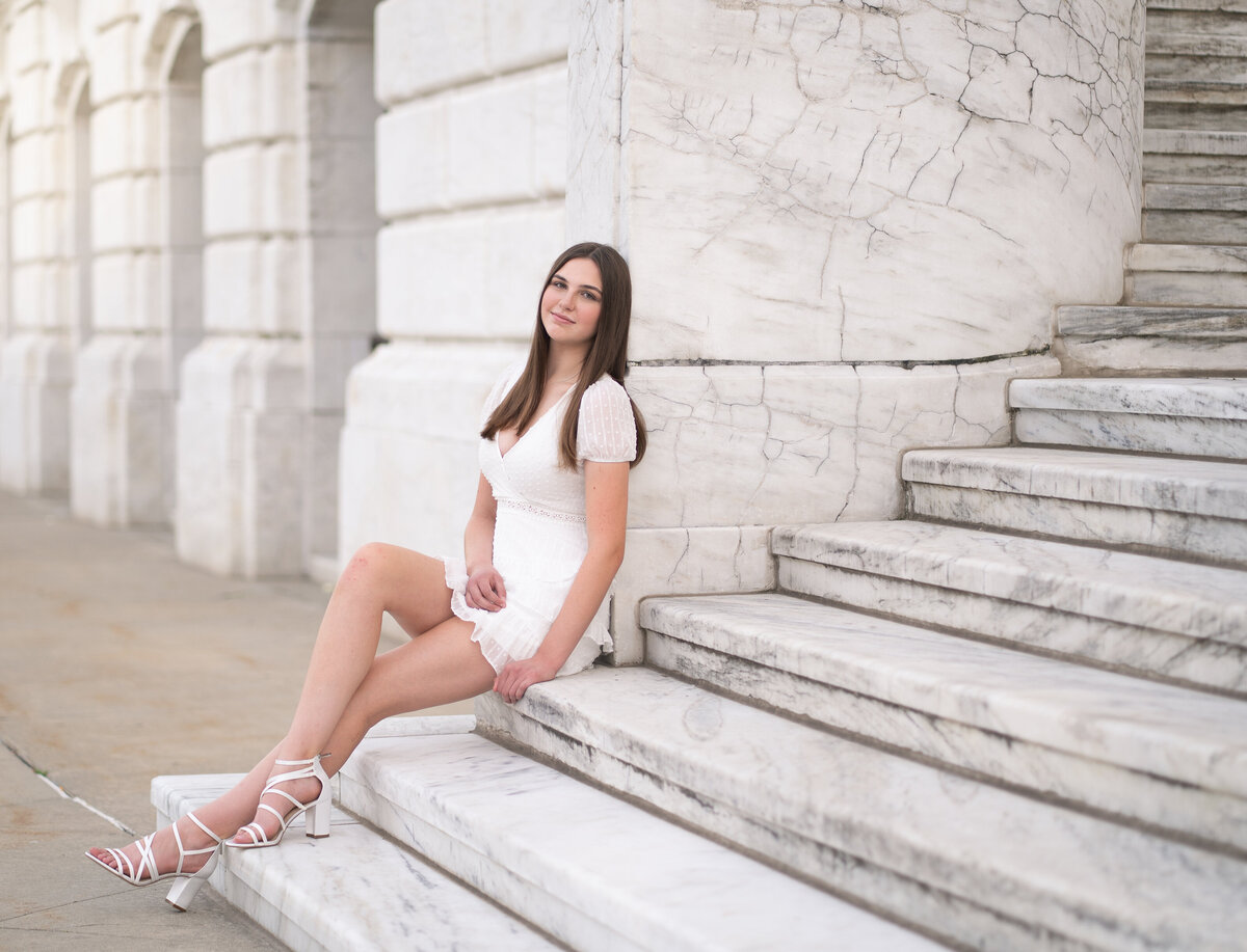 Teenage girl in white dress sitting on white curved staircase of Detroit Institute of Arts building
