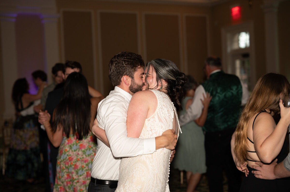 A newlywed couple kissing as they dance with their guests at their reception