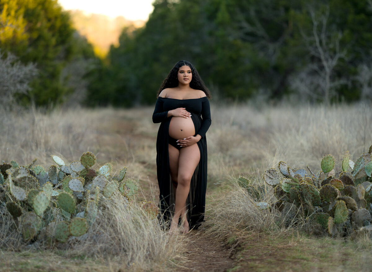 Pregnant woman wearing black open belly dress in a field with cactus