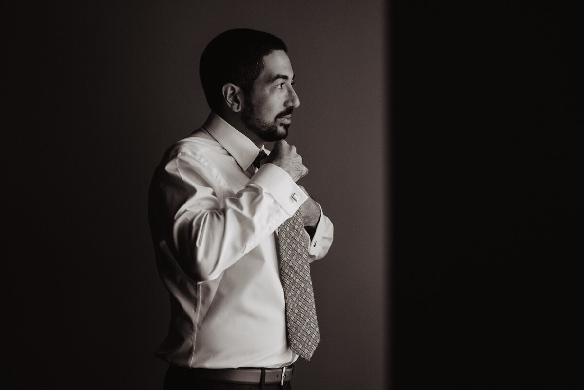 Photographers Jackson Hole capture groom putting on tie in black and white portrait