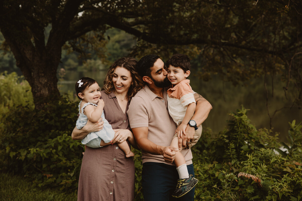 Two parents holding their kids as one kisses their cheek 