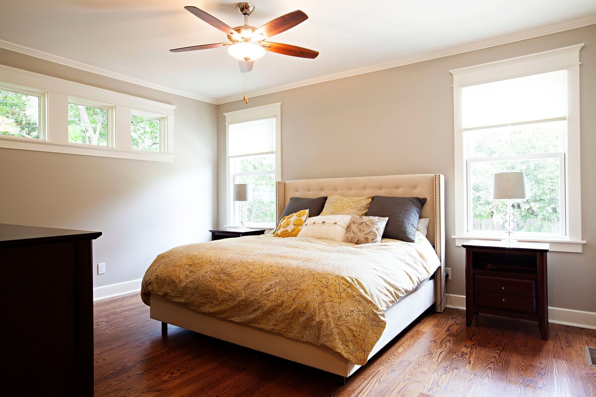 large master bedroom in custom home in central texas. bedroom ceiling fan and large windows behind a beautiful queen bed.