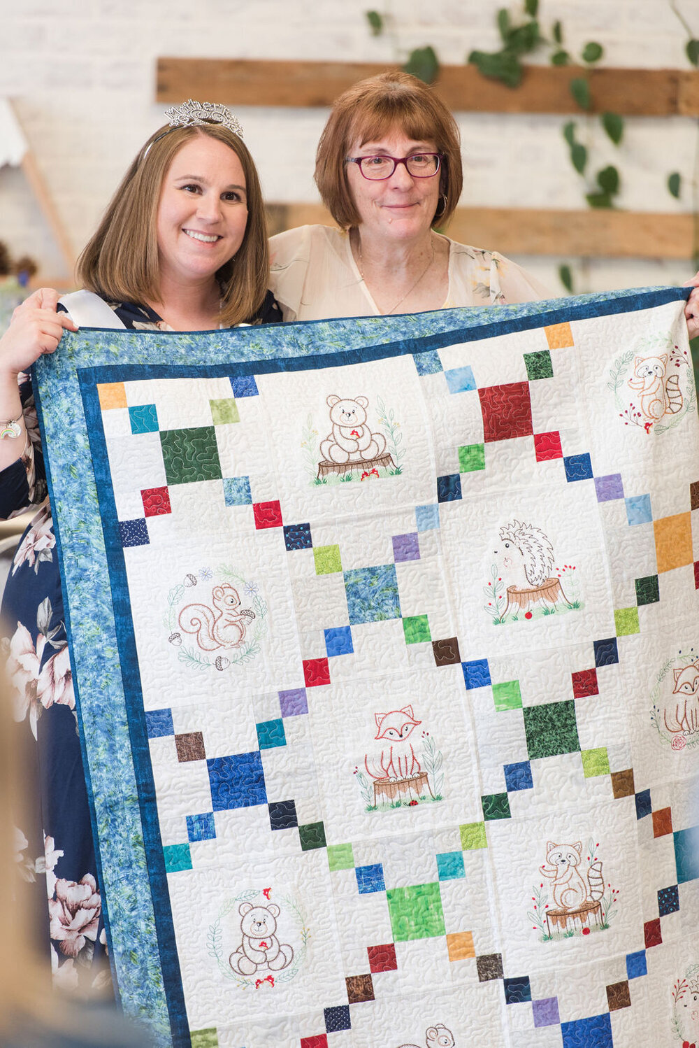 Mom-to-be proudly holding up a woodland-themed quilt made by her aunt as a baby shower gift.