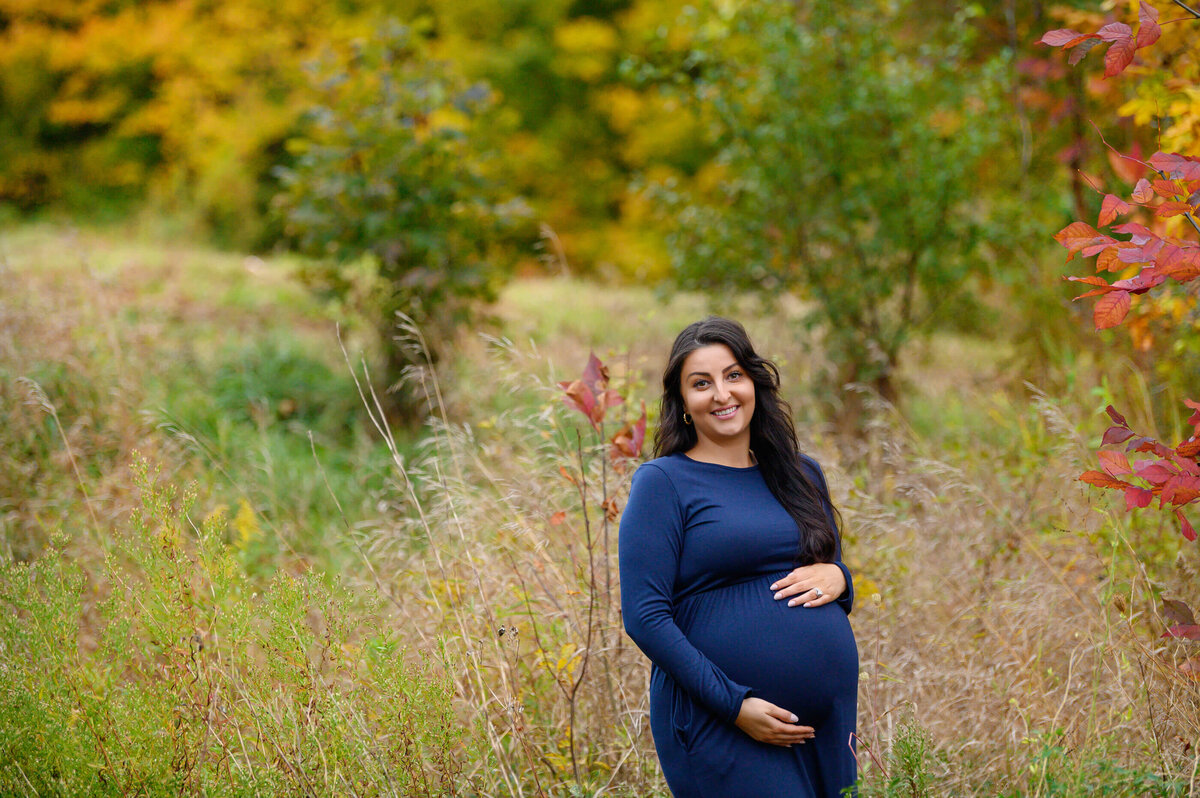 brown-haired pregnant woman wearing a blue maternity dress outdoors for her fall maternity photography session in Burlington, Ontario
