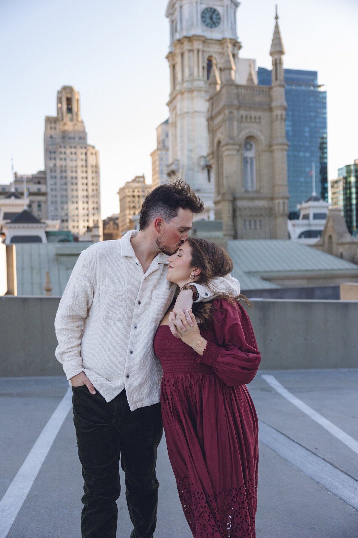Candid rooftop embrace with Philly skyline at sunset.