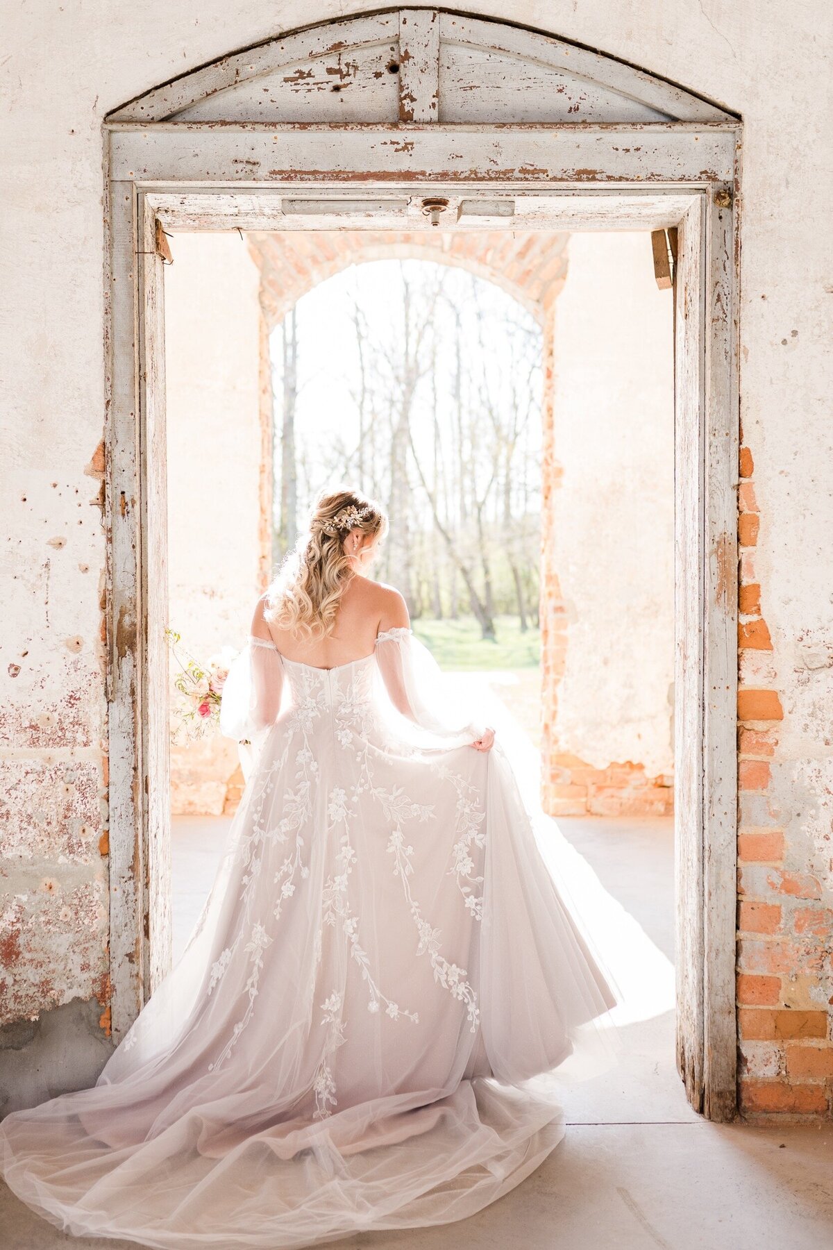 A bride walks through the historic entrance of the Providence Cotton Mill wedding venue and out into the brilliant sunshine in North Carolina.