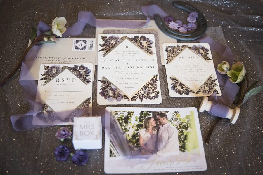 A collection of wedding stationery adorned with purple ribbon, flowers and a horse shoe detail.