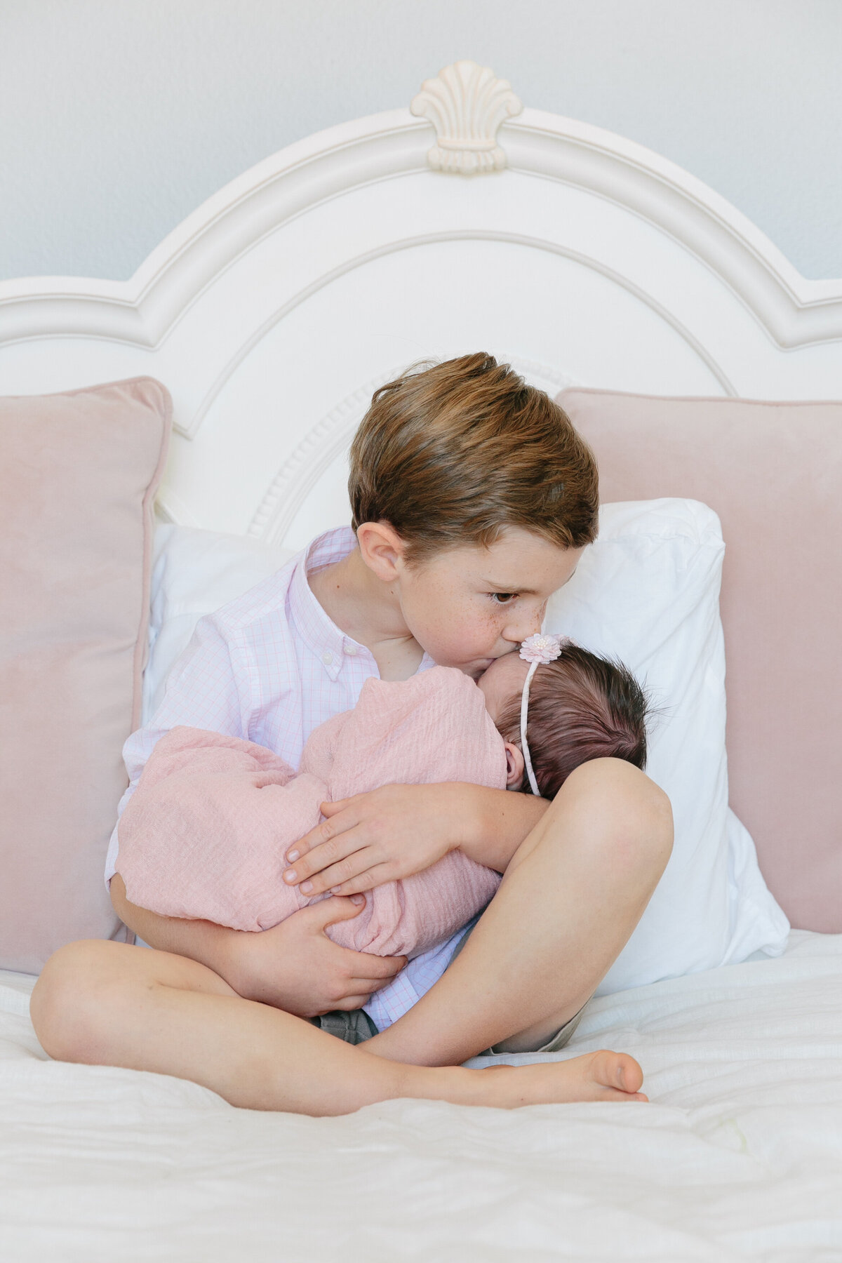 A small boy holding a newborn and kissing their forehead