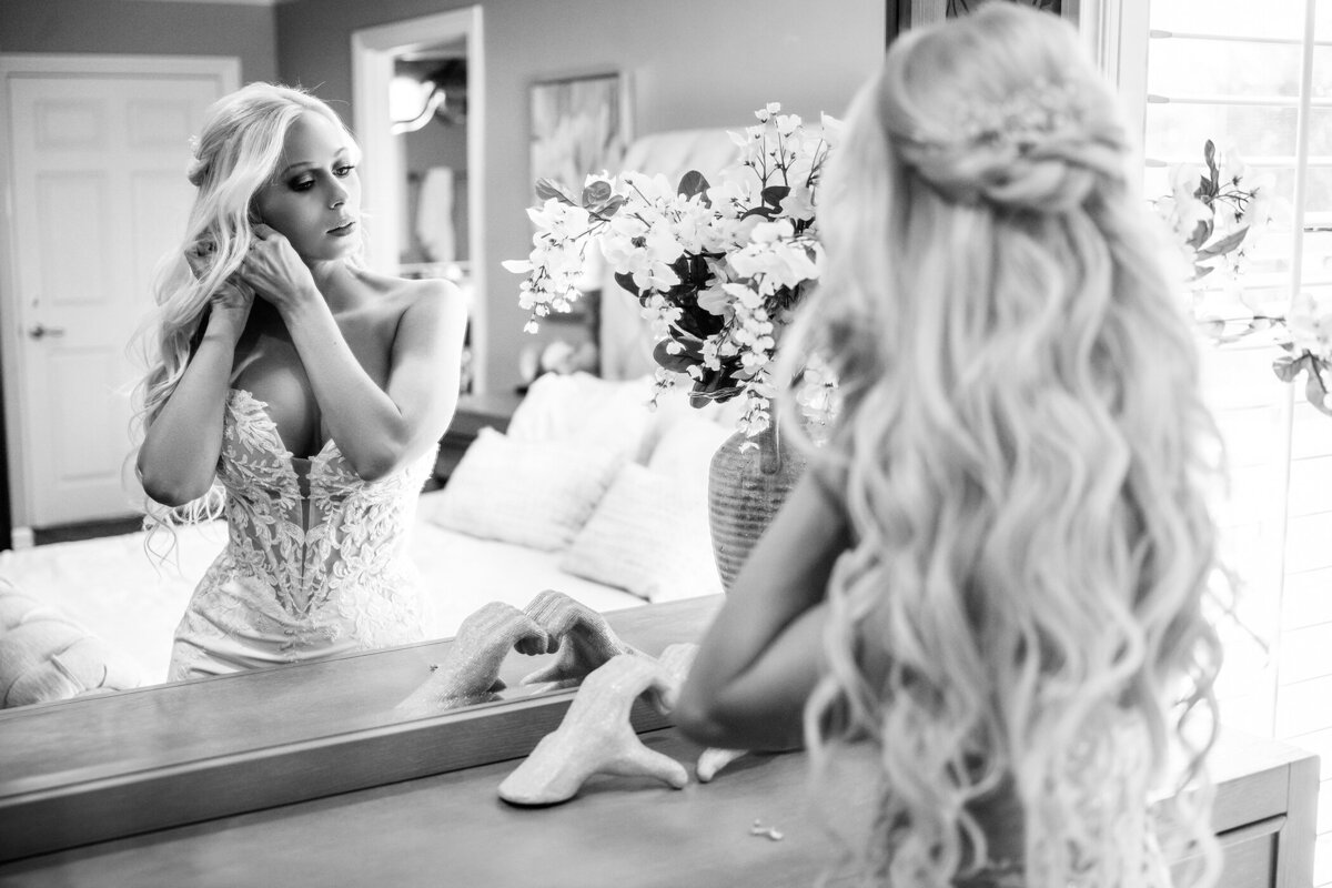 Bride with clip on blond hair extensions putting earrings on in a white form fitted wedding dress