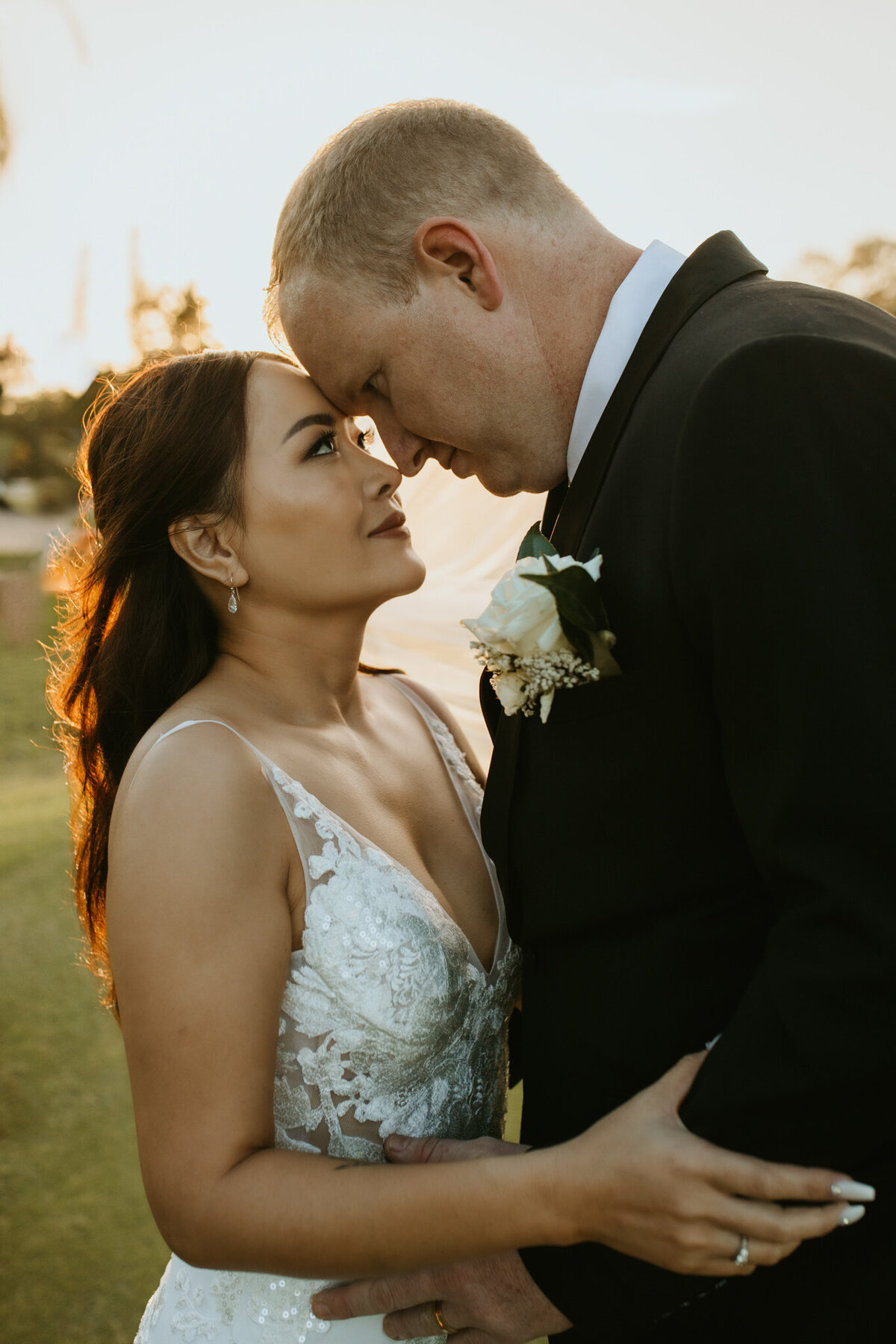 The bride and groom embrace each other while their foreheads touch softly during sunset. 